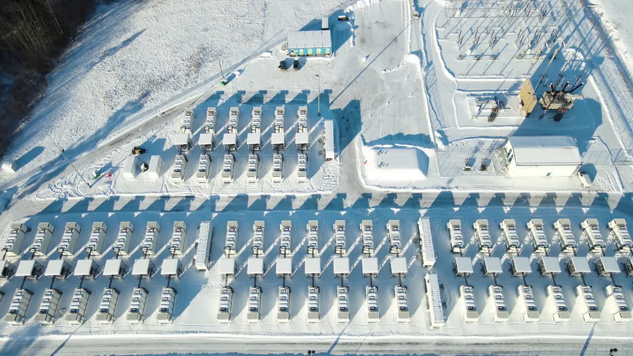 Plynulý letecký oblet ukazuje celý sněhem pokrytý skladovací komplex a elektrické rozvodny podporující spolehlivou dodávku obnovitelné energie.