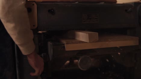 closeup of a male hand pushing a wooden rail through a stationary grinding machine. slow motion