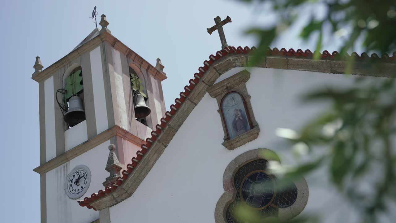 white church with clock tower, bells, and stained glass window framed against blue sky