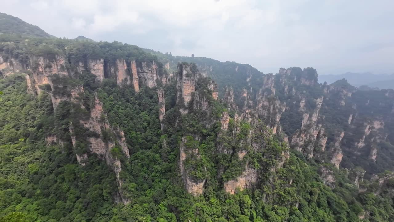 Smooth pan right across green-covered pinnacles of Zhangjiajie mountains during hazy midday light