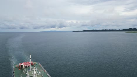 Vista-Aérea-Del-Ferry-De-Pasajeros-Que-Navega-Hacia-Su-Destino-Con-Aguas-Oceánicas-Idílicas-Y-Paisaje-Nublado-En-El-Fondo