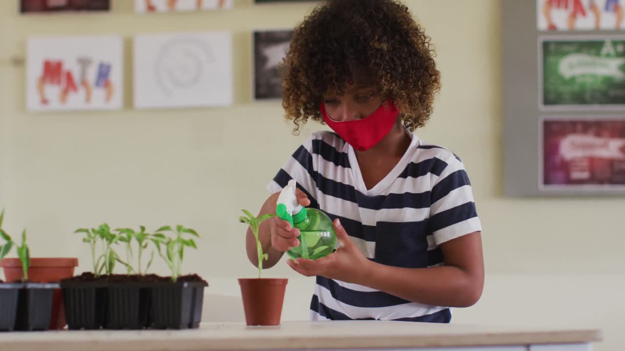 얼굴 마스크 를 착용 한 소년 이 식물  ⁇ 비 에 물 을 뿌리고 있다