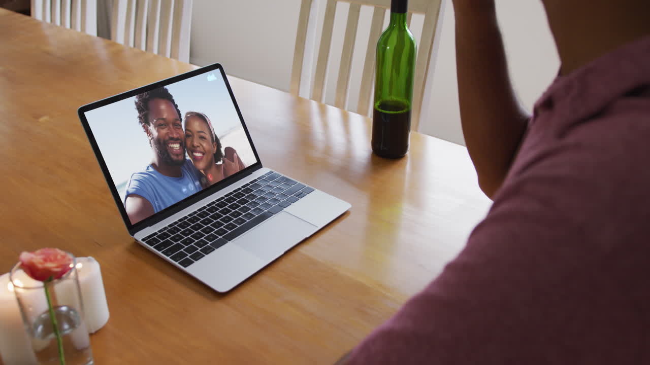 Mid section of african american man drinking wine while having a video call on laptop at home