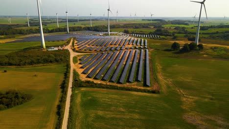 aerial footage of solar panels plant and wind turbines in a wind farm generating green electric energy on a wide green field on a sunny day, in taurage, lithuania