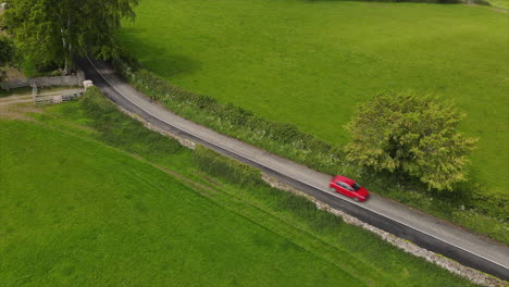 Red-car-passes-by-long-narrow-road-in-Ireland-in-summertime