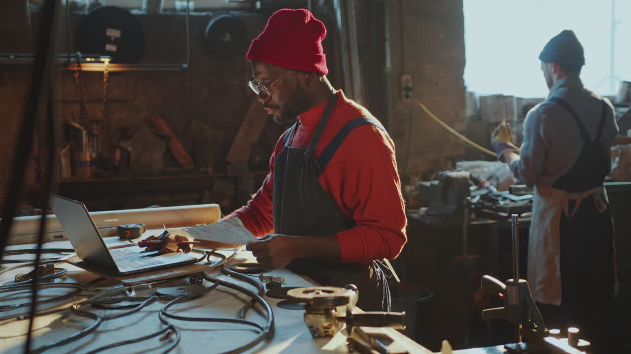 African American Blacksmith Using Laptop and Taking Notes in Workshop