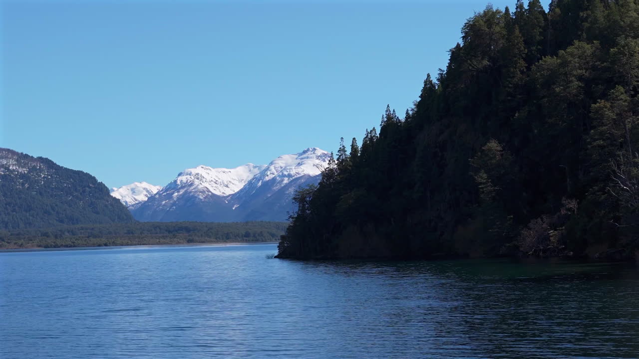 A serene lake with snowy mountain peaks and forested shores in Patagonia