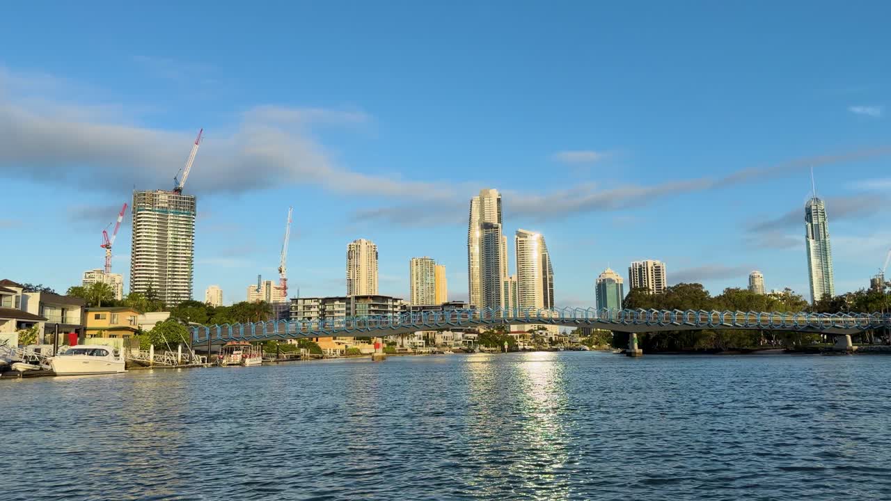 Boat approaches city skyline over river, golden hour lighting, calm water, steady wide shot