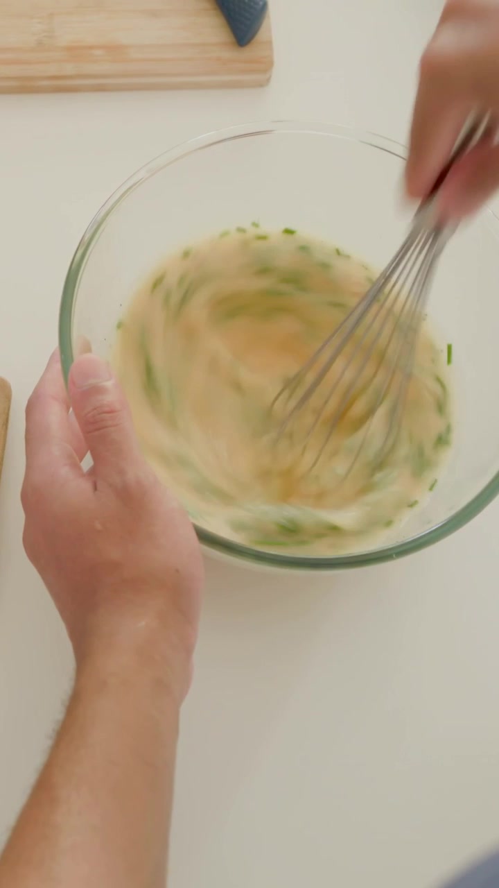 Video verticale: Telecamera che mostra un cuoco che affetta il pane, mescola le uova sul bancone della cucina mentre prepara un pasto, con maglietta blu.