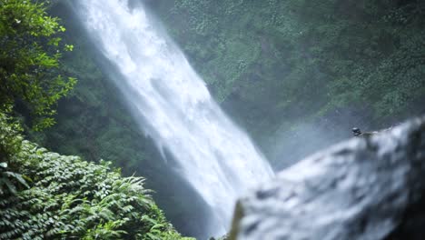 Slow-motion-panning-up-shot-in-front-of-a-gushing-NungNung-Waterfall-in-Bali,-Indonesia-following-a-rain-storm