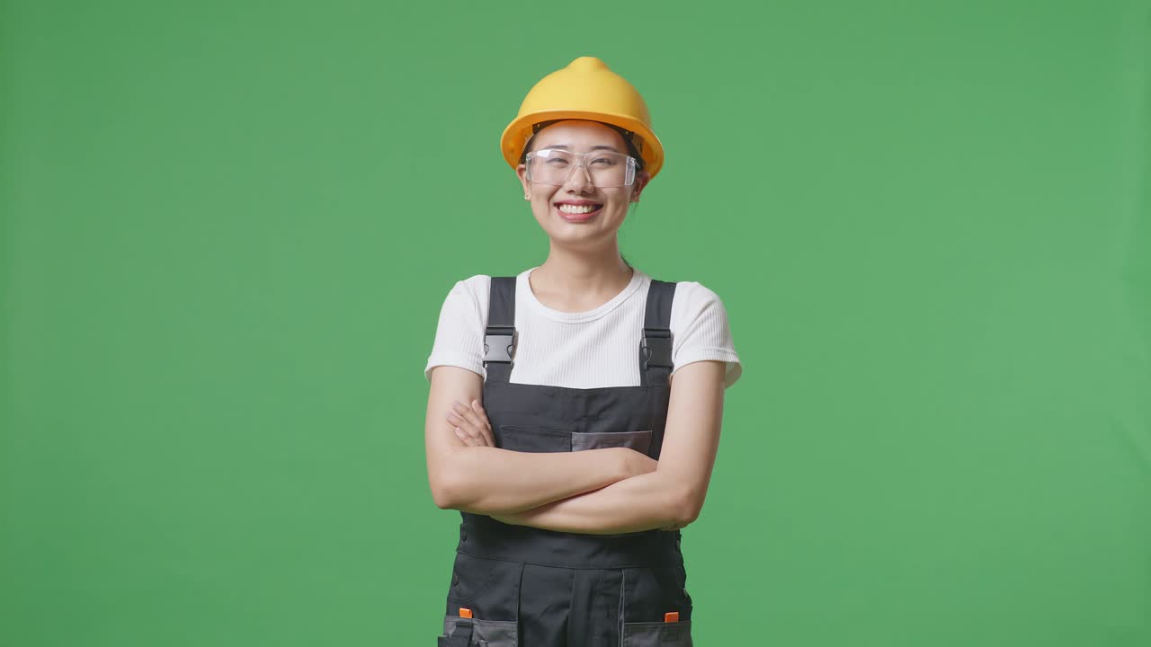 Asian Woman Worker Wearing Goggles And Safety Helmet Smiling And Crossing Her Arms While Standing In The Green Screen Background Studio