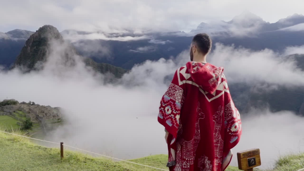 un turista con un poncho rojo observa el paisaje en machu picchu, perú.