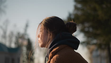 a close-up of a girl wearing a brown coat, with her hair partially covering her face. she looks deeply unhappy and lost in thought. the background is softly blurred