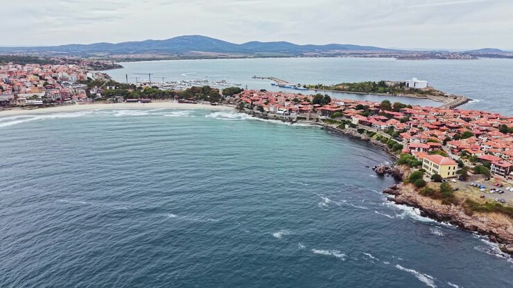 Vista costiera di una piccola città con tetti in tegole rosse e onde che si infrangono sulla riva