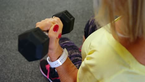 senior woman doing biceps workout with dumbbell in fitness studio 4k