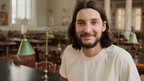 Joven-Estudiante-Sonriendo-A-La-Cámara-En-La-Biblioteca