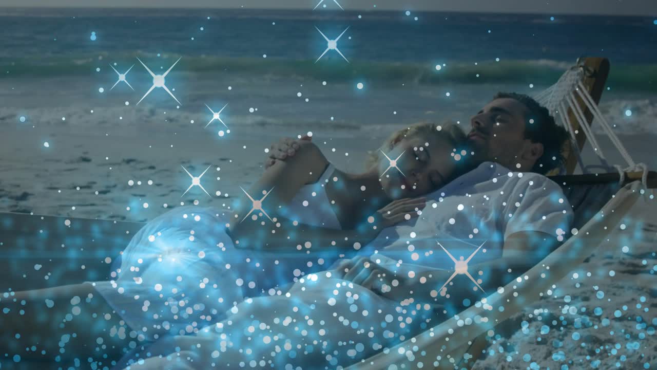 Pareja tomándose de la mano en una hamaca en la orilla, con un atardecer que crea un efecto de brillo de viaje flotando sobre ellos.
