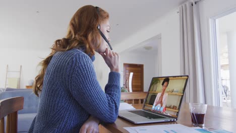 mujer caucásica con auriculares de teléfono haciendo una videollamada con una colega en una computadora portátil en casa