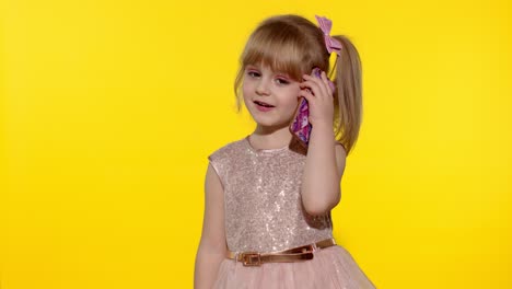 young modern child girl in dress communicates on mobile phone, smiles and talks. yellow background