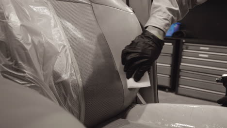 Ingeniero-Profesional-Con-Guantes-Negros-Usando-Expertamente-Una-Esponja-De-Espuma-Para-Limpiar-El-Asiento-De-Cuero-Del-Auto