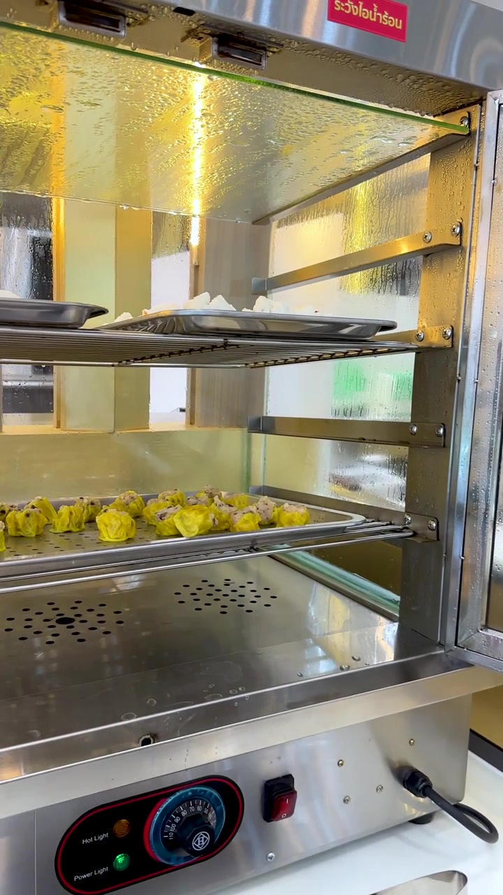 Una persona usa delle pinze metalliche per prendere panini al vapore e shumai da uno scaldavivande in vetro