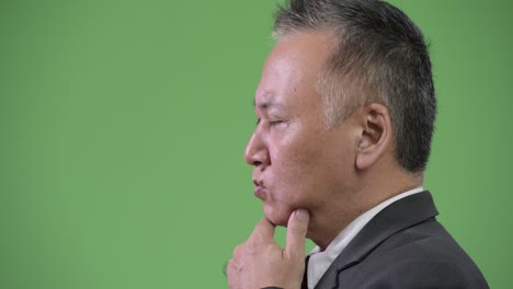 profile view of mature japanese businessman thinking against green background