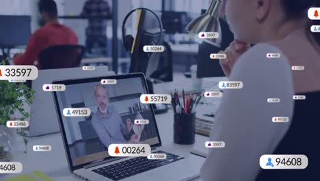 Animation-Von-Social-Media-Symbolen-Vor-Einer-Kaukasischen-Frau,-Die-Im-Büro-Einen-Videoanruf-Auf-Einem-Laptop-Führt