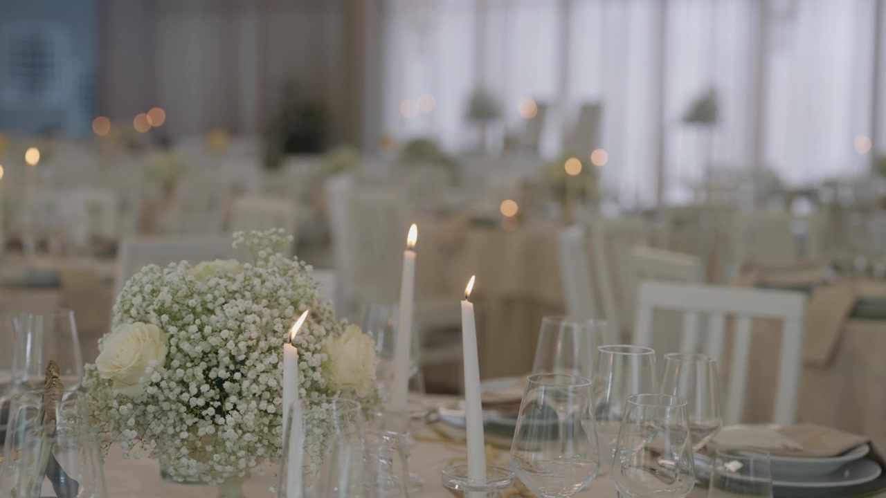 Elegante tavolo da ricevimento nuziale con centrotavola di fiori bianchi, candele accese e cristalleria.