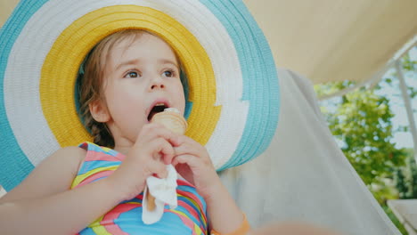 a little girl in a big hat enjoys eating ice cream with pleasure 4k video