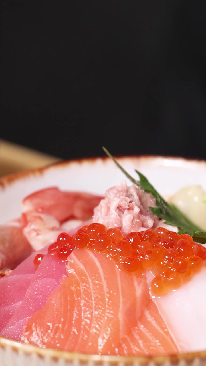 Primo piano di uno chef che usa le bacchette per disporre sashimi fresco su una ciotola di riso