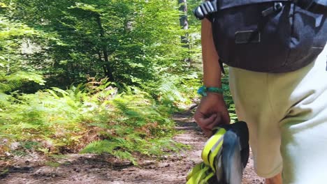 close up following young boy walking trough woods with climbing shoes swinging