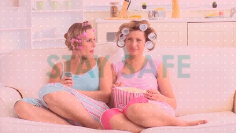 animation of social distancing message over two caucasian woman eating popcorn