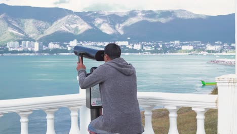 man looking through binoculars at coastal view