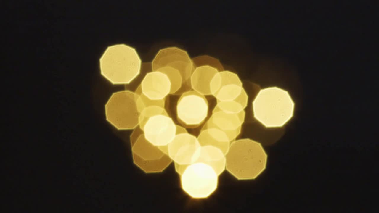 Die Kamera zieht den Fokus und enthüllt ein goldenes Herzornament in einem dunklen Studio, das warme Bokeh-Lichter reflektiert