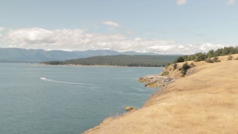 de pie en el borde del acantilado de la pradera de helliwell contemplando la costa, con montañas al fondo y un barco a motor navegando por el océano en la isla hornby en columbia británica, canadá.