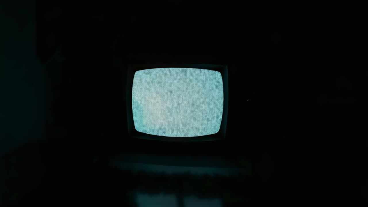 Activating CRT television displaying flickering static noise in dark room, with interference