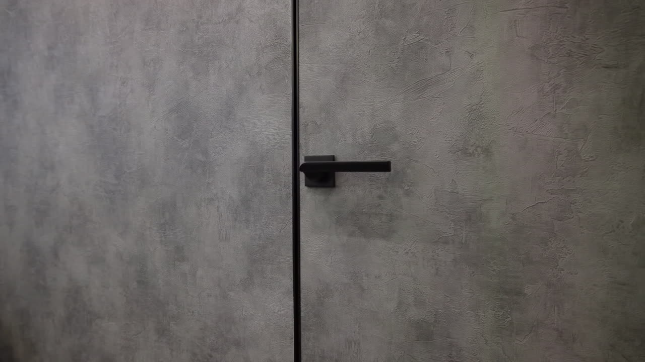 Primo piano: porta interna in cemento con maniglia nera, pannello testurizzato opaco in tonalità di grigio tenui, set di maniglie a leva elegante