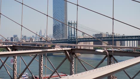 slow motion landscape of wires arches of brooklyn bridge with manhattan structure cargo freight barge on east river new york city skyline skyscraper buildings usa america travel tourism