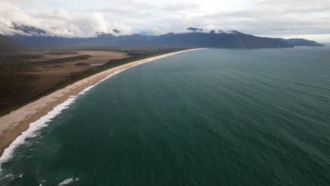 sandy beach on bruce bay in south island, new zealand, with ocean waves and distant mountain on sunny day. aerial shot