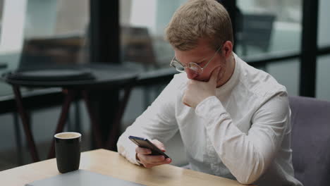 Adult-businessman-texting-on-smartphone-while-sitting-by-laptop