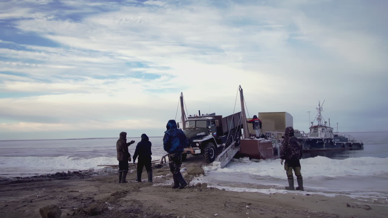 트럭과 화물선이 얼어붙은 북극 해변에서 배를 내리고 있습니다.