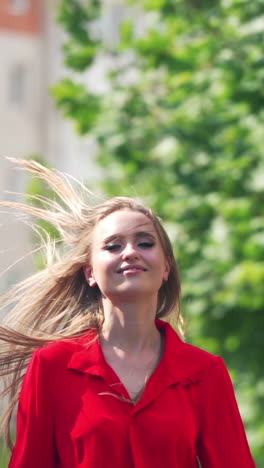 Front view of a smiling woman. Beautiful female in red passionate dress runs on the street in the city. Happy girl with long hair in move. Slow motion. Vertical video