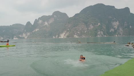 man jumping and swimming in a scenic lake amidst mountains