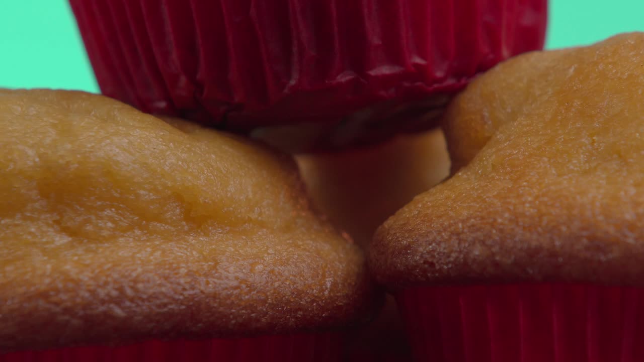 Close-up of a pyramid of golden tamales cupcakes, some wrapped in vibrant red paper cups, creating a visually appealing arrangement against a turquoise backdrop