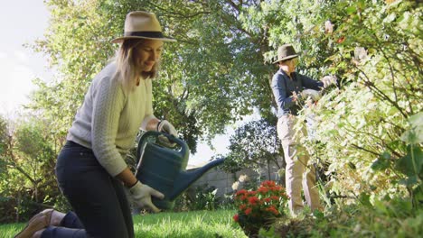 pareja de lesbianas caucásicas con sombreros haciendo jardinería juntos en el jardín