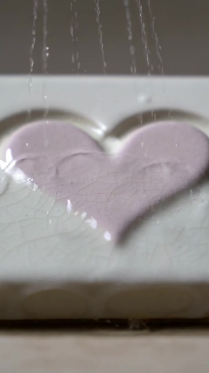 Video verticale: Raccoglie un cuore rosa pallido su una piastrella smaltata, mentre getti d'acqua che cadono creano un luccichio.
