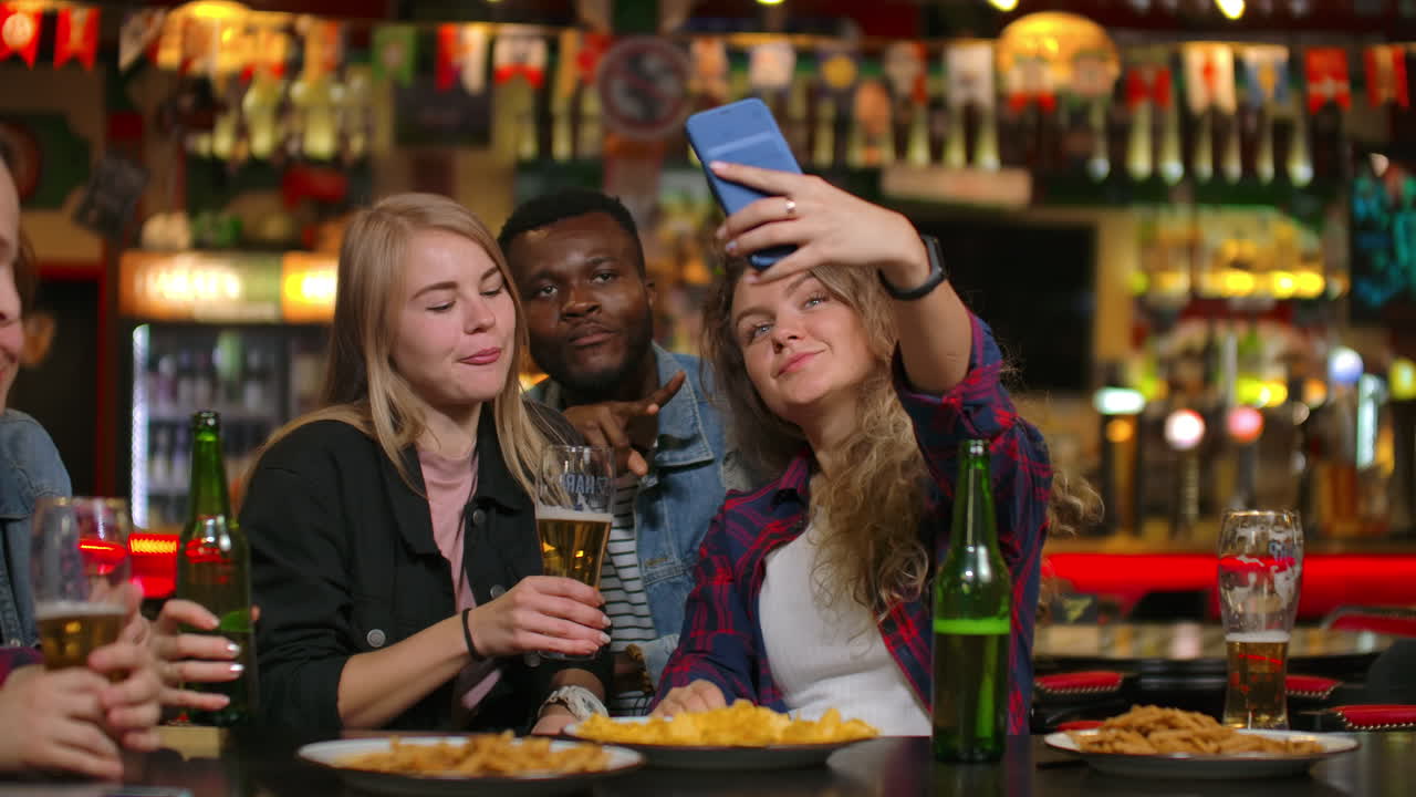 Un gruppo di amici eterogenei si fa un selfie con il cellulare in un bar.