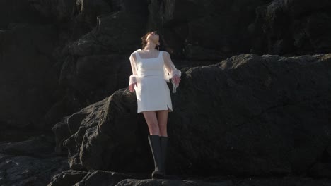 Stunning-Woman-In-White-Square-neck-Dress-With-Sheer-Sleeves-Gracefully-Strolls-On-Beach-Rocks-With-Elegance-And-Poise