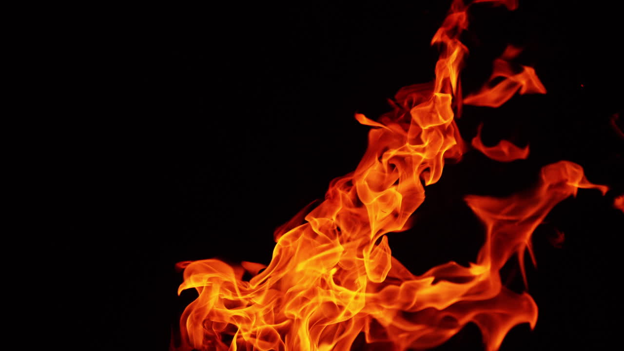 Long fire flame stretching into the air in the dark night. Tine sparks flash in the darkness.