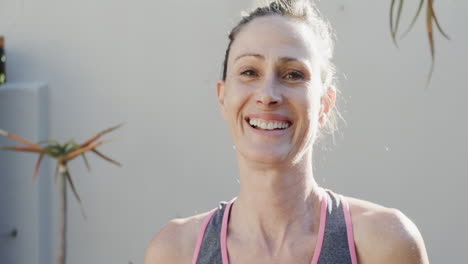 Portrait-of-happy-unaltered-senior-caucasian-woman-smiling-in-front-of-wall-and-plants,-slow-motion